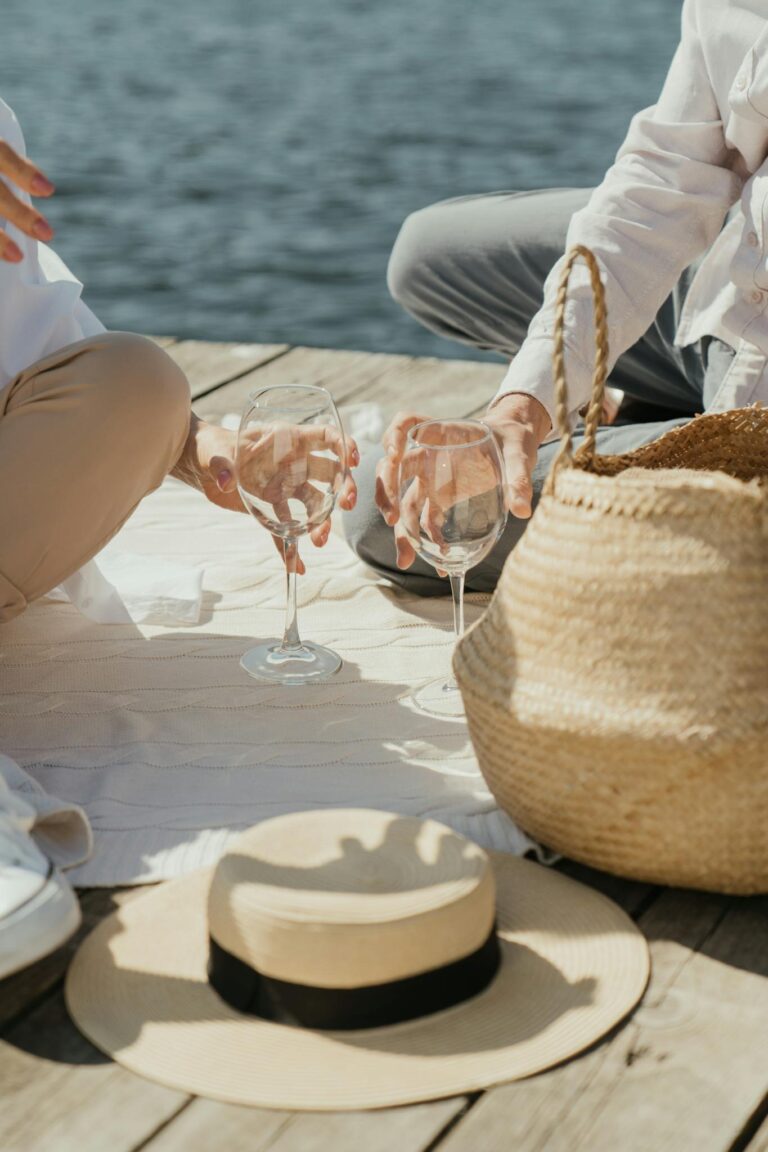 Couple enjoying a romantic picnic with wineglasses on a pier by the water.