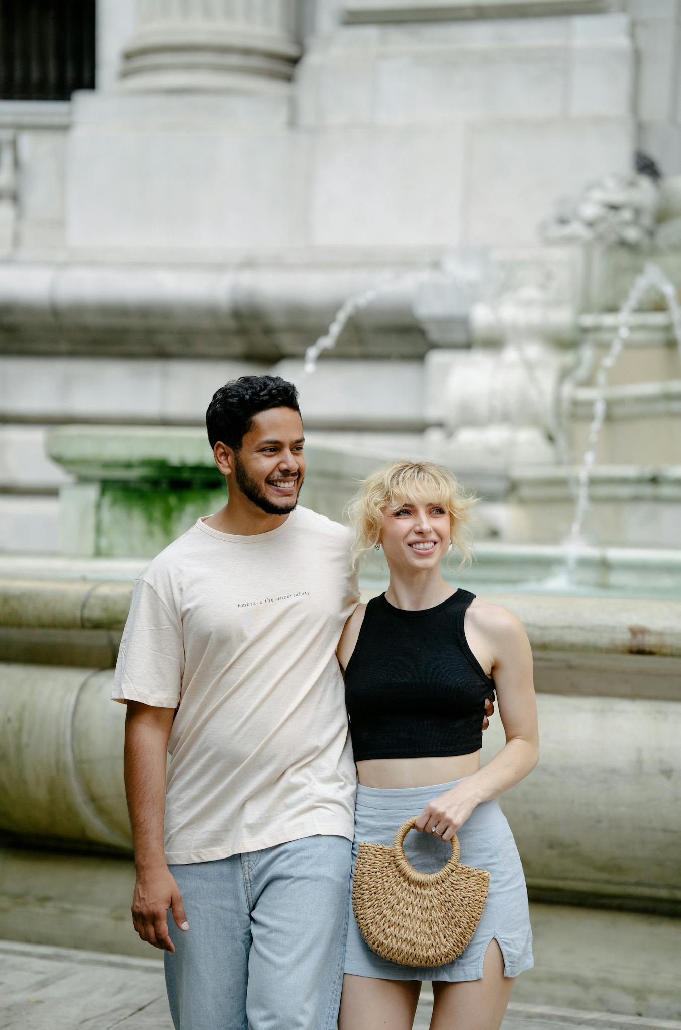 Smiling couple standing together by a fountain outdoors, exuding joy and connection.