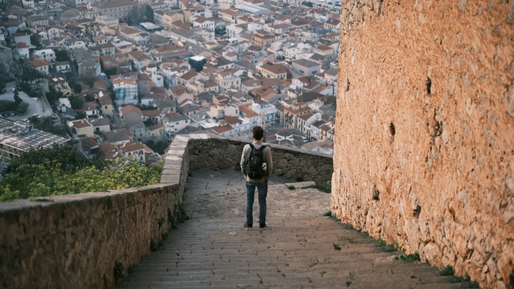 Ein Mann steht mit dem Rücken zur Kamera auf einer breiten Steintreppe. Er blickt über eine südliche Stadt, zu der die Stiege hinabführt.