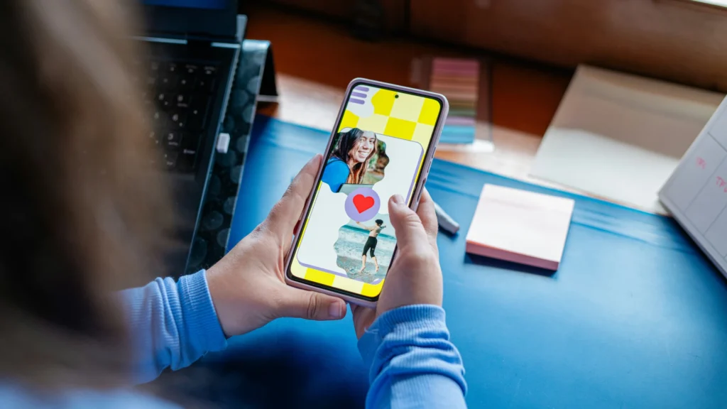 Der Blick geht über die rechte Schulter einer Frau, die ein Smartphone mit geöffneter Dating-App in den Händen hält.