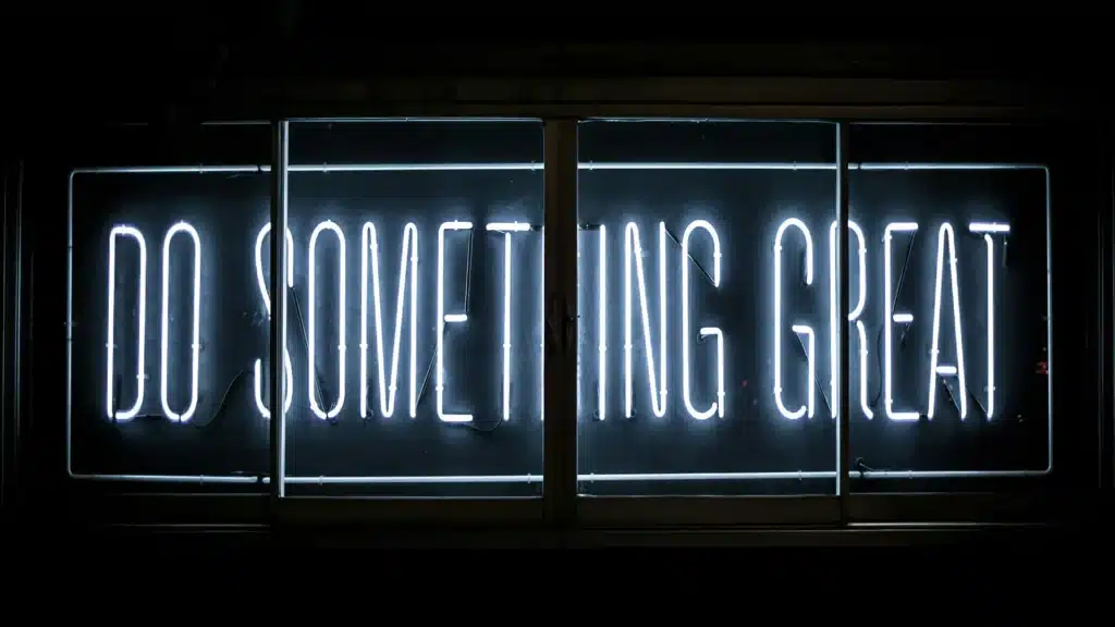 Vor schwarzem Hintergrund hängt die weiß leuchtende Neonschrift "Do something great" in Großbuchstaben.