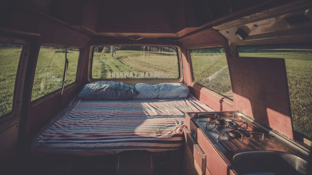 Der Innenraum eines Campingbusses. Vorn rechts eine kleine Küchenzeile, dahinter ein Längsbett über die gesamte Fahrzeugbreite.