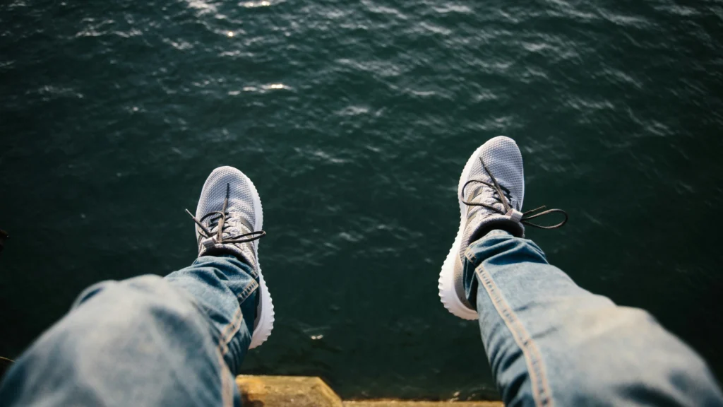Zwei Beine in Blue Jenas und Turnschuhen baumeln hoch über dem Wasser.
