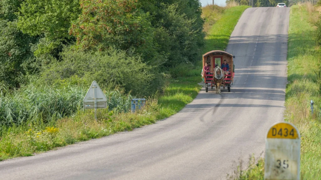 Ein hölzernes, einspänniges Pferdefuhrwerk mit zwei Leuten auf dem Bock rollt eine Straße hinab.