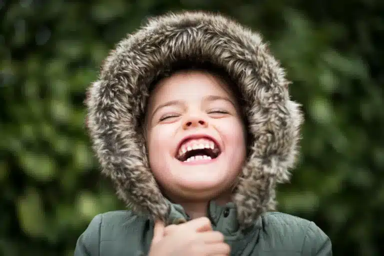 Eone jubelnde junge Frau. Sie trägt einen Parka mit pelzbesetzter Kapuze.