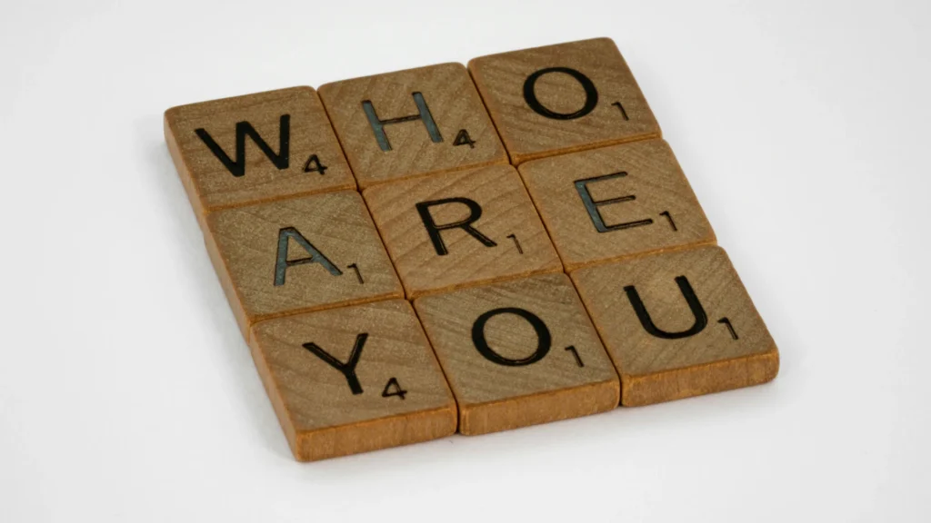 In Holz gravierte schwarze Großbuchstaben bilden den Schriftzug "Who are you".