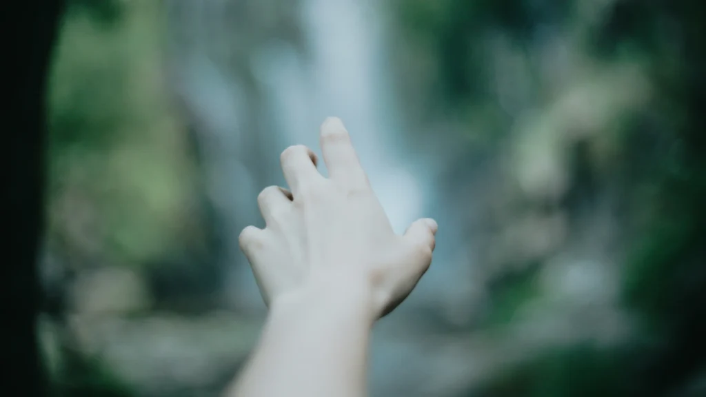 Eine Hand reckt sich von vorn ins Bild. Der Hintergrund ist schemenhaft.