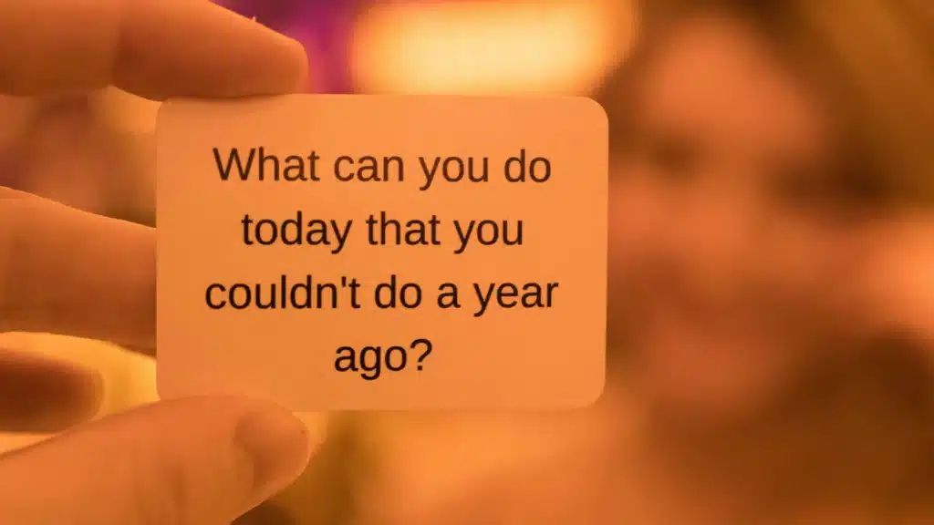 Eine Hand hält eine Karte mit der Aufschrift "What can you do today that you couldn't do a year ago?" in die Kamera.