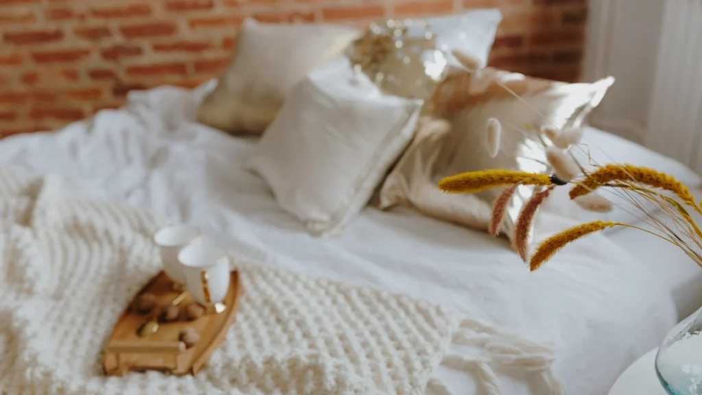 Ein Holztablett mit Tassen und Löffel auf einem Bett. Von rechts ragen Ähren ins Bild.