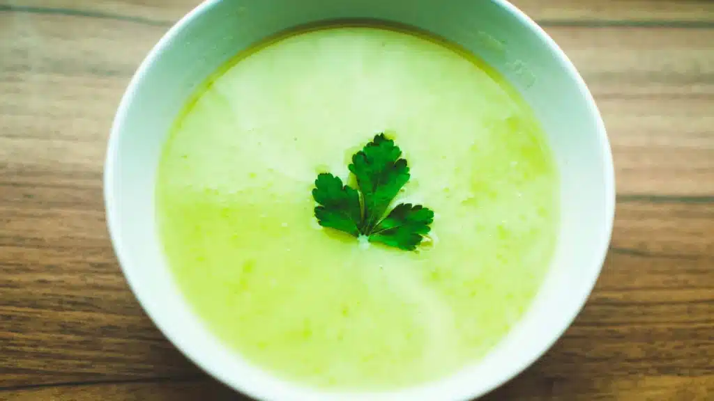 Ein Teller mit Gurksuppe steht auf einer hölzernen Tischplatte.