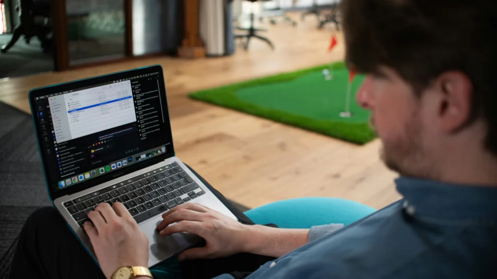 Ein Mann sitzt mit einem Laptop auf dem Schoß auf dem Boden seiner Wohnung.