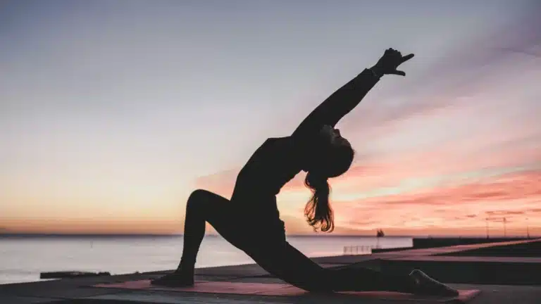 Eine Frau macht bei Tagesanbruch eine Yogaübung an einem Strand.