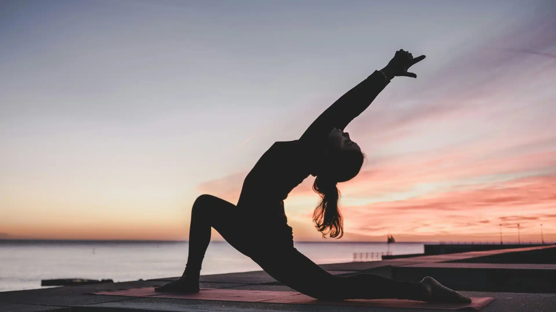 Eine Frau macht bei Tagesanbruch eine Yogaübung an einem Strand.